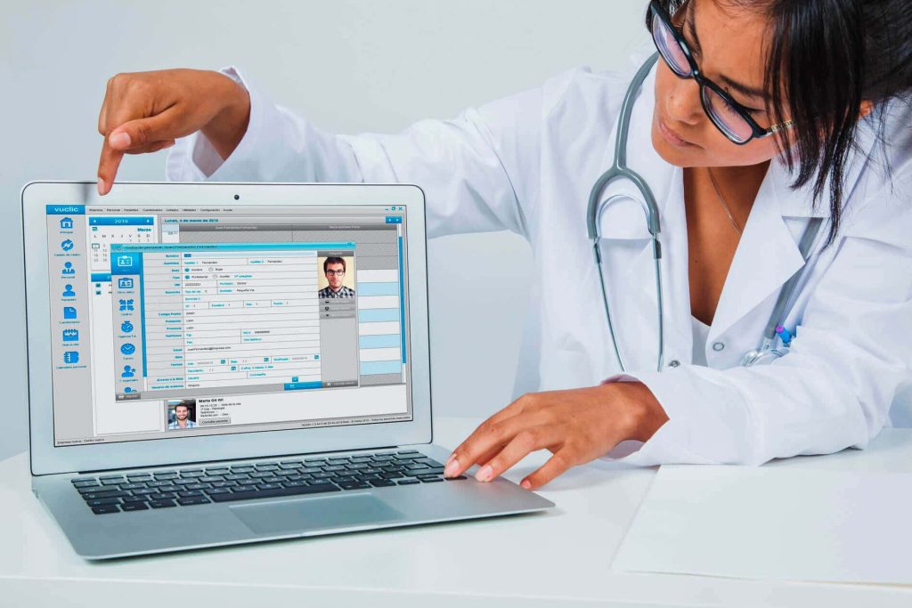 Especialista médica mostrando el historial clínico digital de un paciente en la interfaz del programa Vuclic desde un portátil